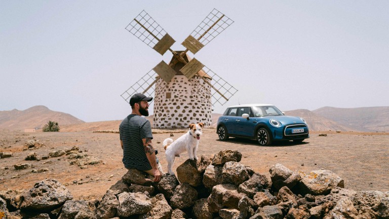 Uros and Paya sitting on stones next to their MINI in front of a windmill.