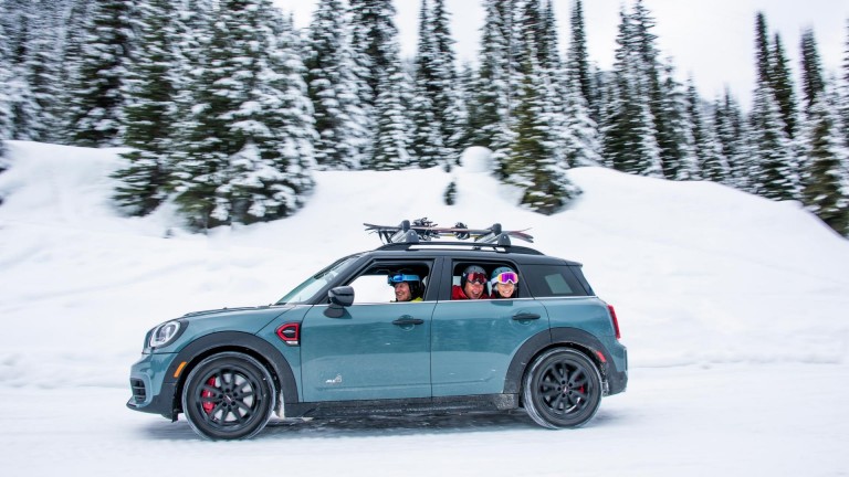 MINI Countryman на заснеженной дороге и члены группы лыжников, выглядывающие из окна. 